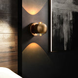 Gold orb sconce lit beside a mirror on a dark wood panelled wall