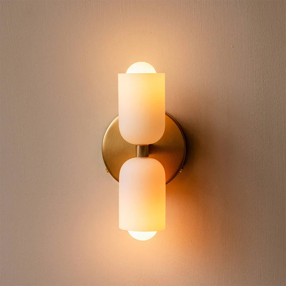 Brass up and down wall light lit, casting warm cones on a pale wall