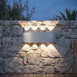 Silver up and down wall light casting scalloped beams across a stone wall