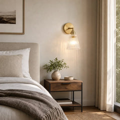 Brass wall sconce lit above a bedside table in a calm bedroom