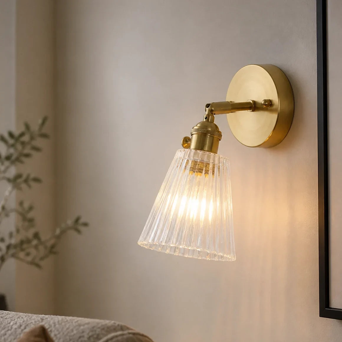 Ribbed glass wall sconce angled down on a cream wall beside a mirror