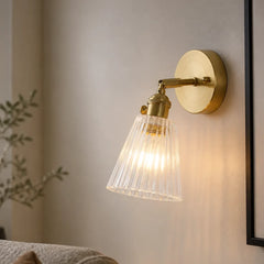 Ribbed glass wall sconce angled down on a cream wall beside a mirror