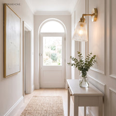Brass wall sconce lighting a bright hallway beside an arched front door