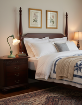 Flower table lamp glowing on a carved nightstand beside a dark four poster bed