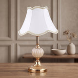 White bell fabric shade on a gold fluted glass base table lamp