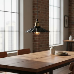 A black scalloped metal pendant light with a brass-toned socket hangs over a wooden dining table in a bright, modern room with brick columns and large windows.
