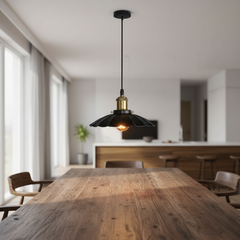 A modern black pendant light with a brass-toned collar and glowing bulb, hanging above a wooden dining table in a bright, contemporary kitchen and dining room.