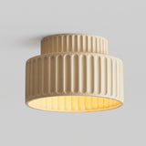 Beige two-tier fluted resin ceiling light lit from within against a plain grey background