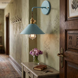 Blue cone shade sconce lit in a hallway above a side table