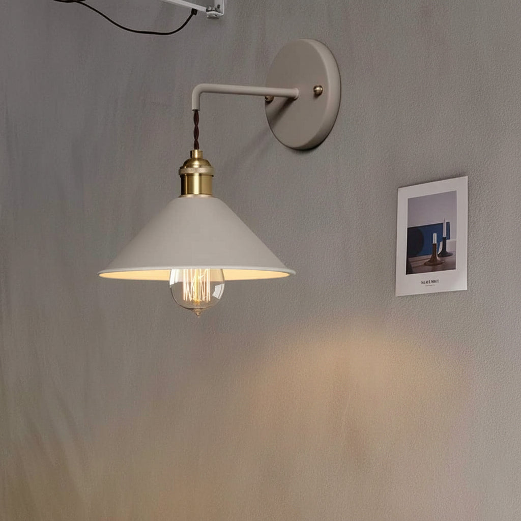 White cone shade sconce lit on a plain wall beside a photograph