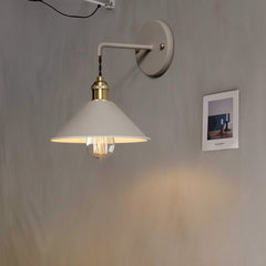 White cone shade sconce lit on a plain wall beside a photograph