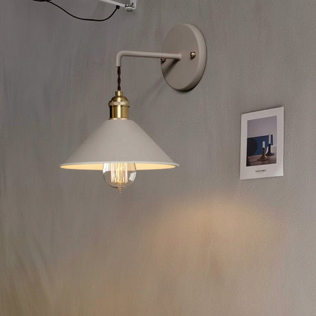 White cone shade sconce lit on a plain wall beside a photograph
