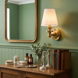 Pleated shade sconce mounted on patterned wallpaper beside flowers