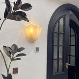 Frosted glass wall sconce beside an arched entry door with foliage