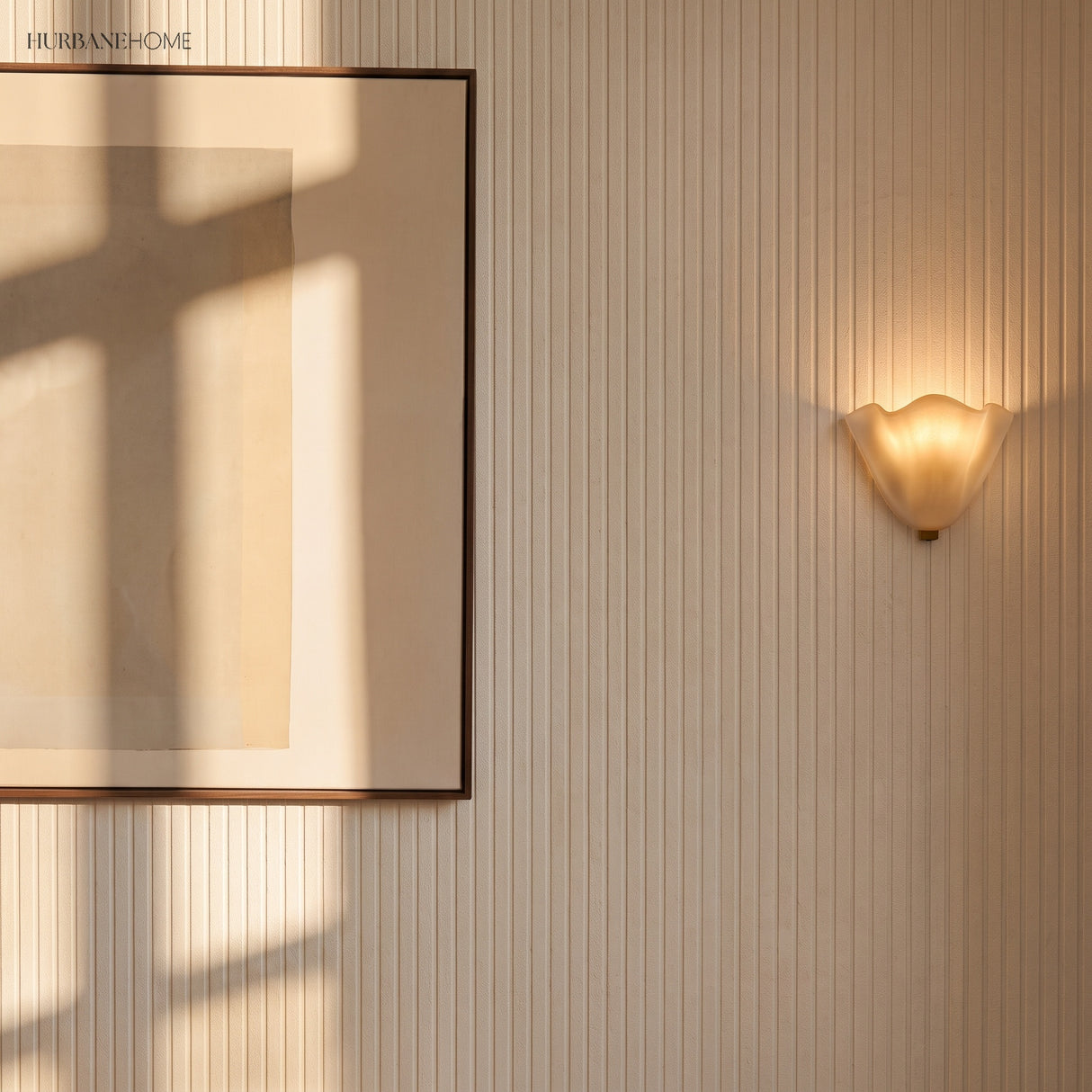 Frosted glass wall sconce on a fluted wall beside framed art in daylight
