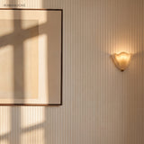 Frosted glass wall sconce on a fluted wall beside framed art in daylight