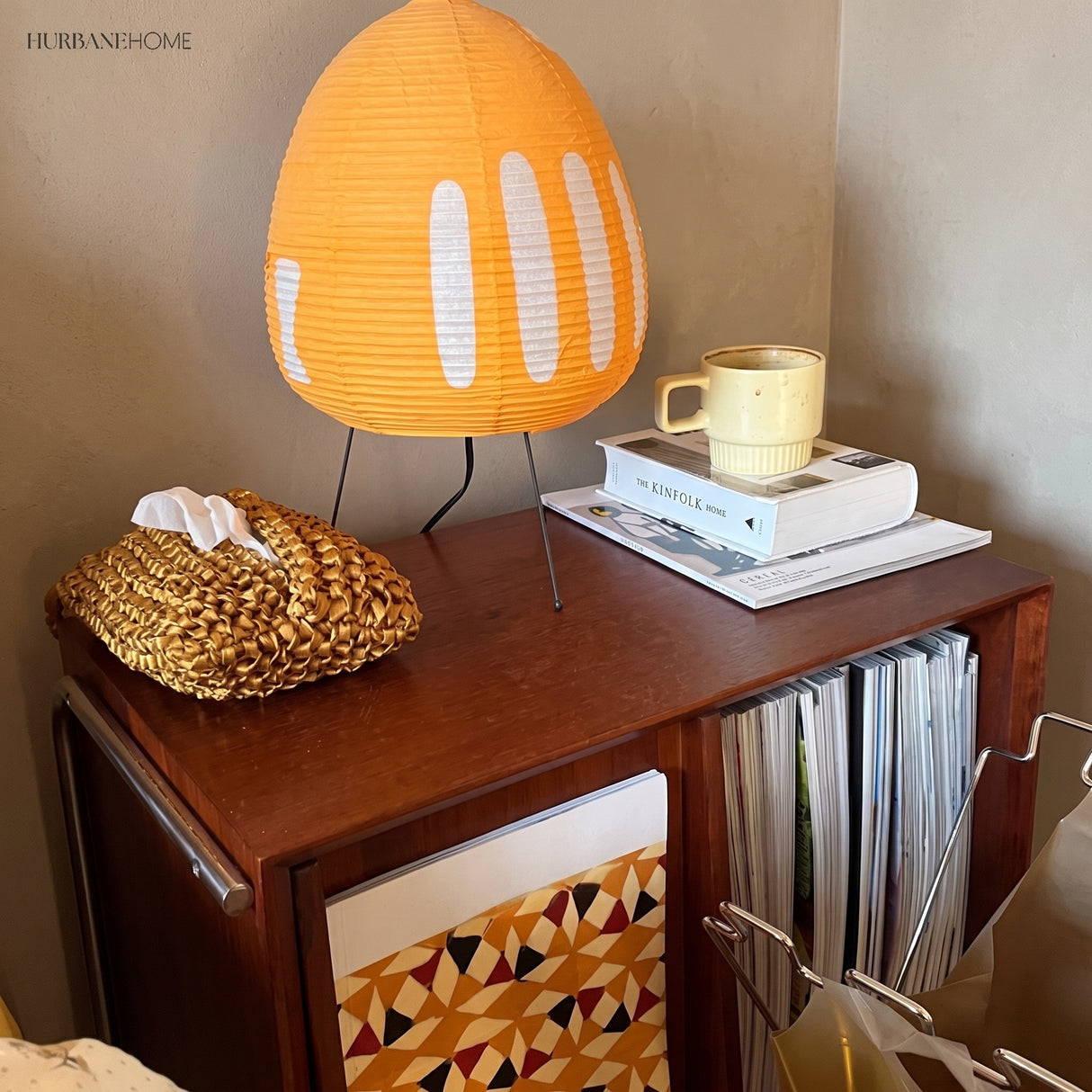 Orange rice paper table lamp on a timber cabinet beside a mug and books