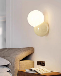 Wall sconce lit above a bedside table with an open magazine and a headboard
