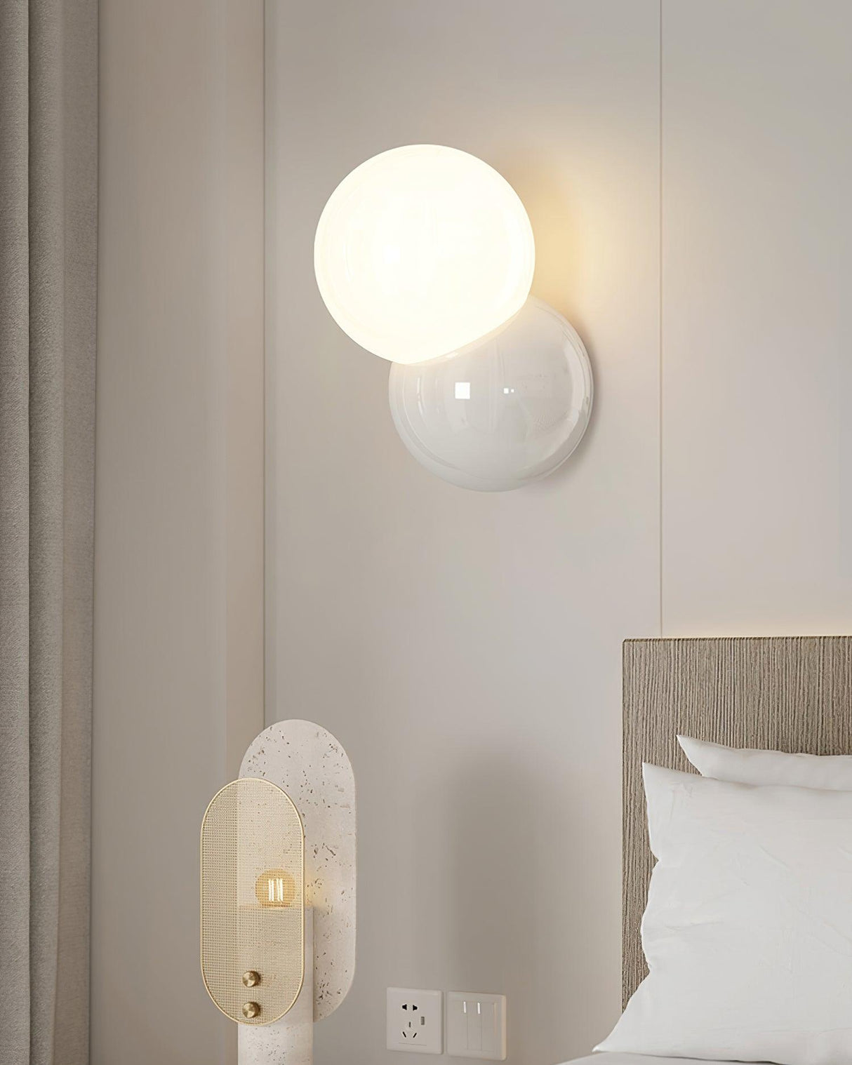Wall sconce mounted low beside a bed next to a wall socket and switch plate