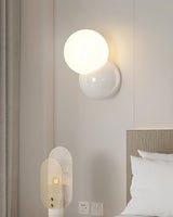 Wall sconce mounted low beside a bed next to a wall socket and switch plate
