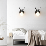 Two black antler sconces lit on a white brick bedroom wall