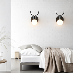 Two black antler sconces lit on a white brick bedroom wall