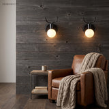 Two black antler sconces lit on a timber clad wall above an armchair