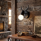 Black antler sconce lit on timber panelling beside a stone fireplace