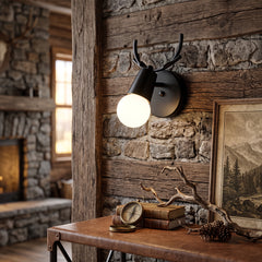 Black antler sconce lit on timber panelling beside a stone fireplace