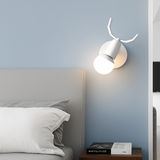 White antler sconce lit on a pale blue wall beside a bed