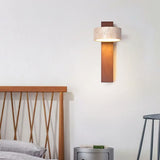 Walnut travertine wall sconce glowing above a wooden bed and round side table