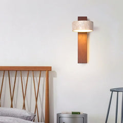 Walnut travertine wall sconce glowing above a wooden bed and round side table