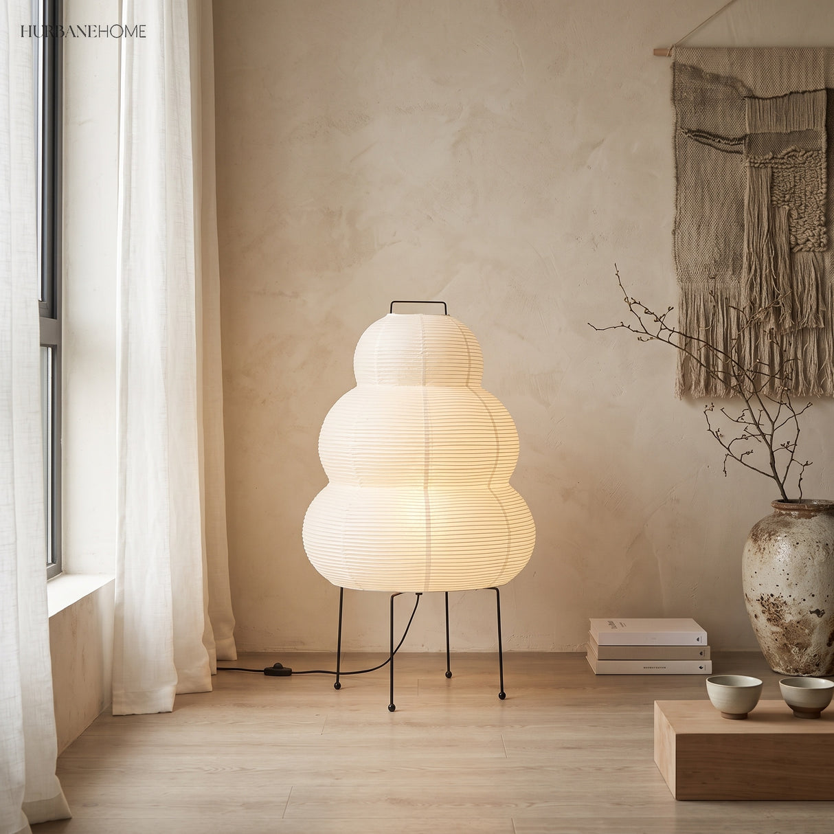 Lit rice paper floor lamp by a curtained window with a ceramic vase