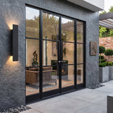 Black waterproof outdoor wall light beside black-framed glass doors on stone wall