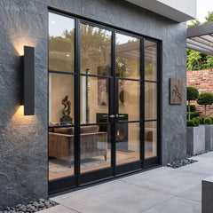 Black waterproof outdoor wall light beside black-framed glass doors on stone wall