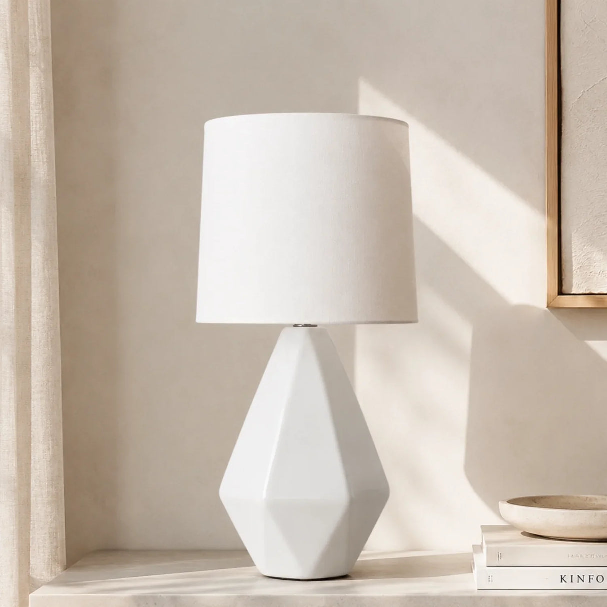 Faceted white ceramic table lamp with drum linen shade in sunlit room