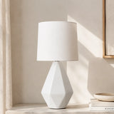 Faceted white ceramic table lamp with drum linen shade in sunlit room