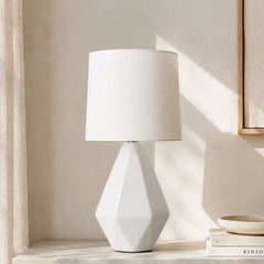 Faceted white ceramic table lamp with drum linen shade in sunlit room