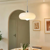 White glass pendant light by pale curtains above a table with orange chairs