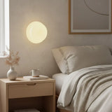Lit white glass wall sconce beside a bed with oak nightstand