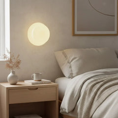 Lit white glass wall sconce beside a bed with oak nightstand