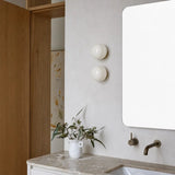 Two white glass wall sconces stacked beside a bathroom vanity mirror