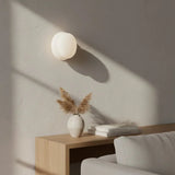 White globe glass wall sconce casting soft shadow on plaster wall