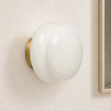 White opal glass wall sconce with brass base on cream wall