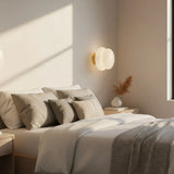White opal glass wall sconce beside bed with brass base and dried grass