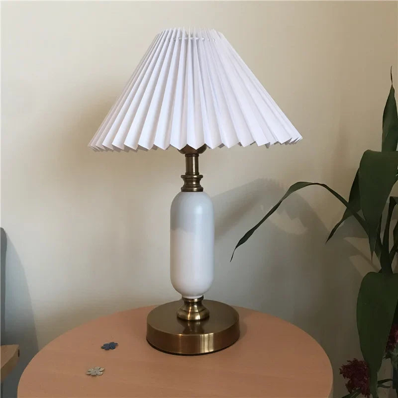 White pleated table lamp beside a green plant