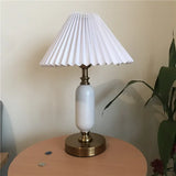 White pleated table lamp beside a green plant