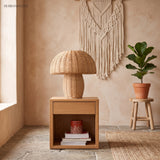 Rattan table lamp on an oak nightstand with a macrame wall hanging behind
