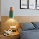 Green cylinder pendant lit above a bed and timber headboard