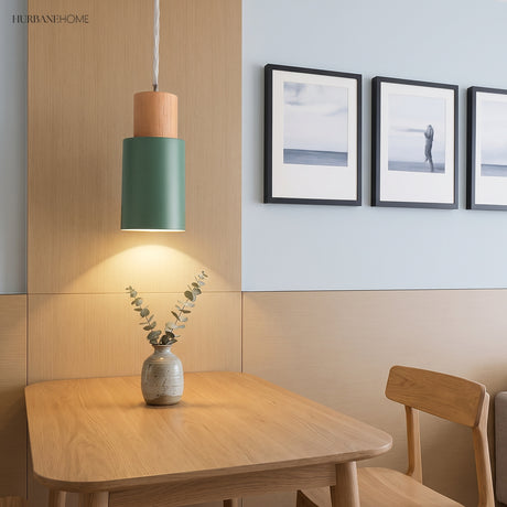Green cylinder pendant lit above a wooden dining table and vase